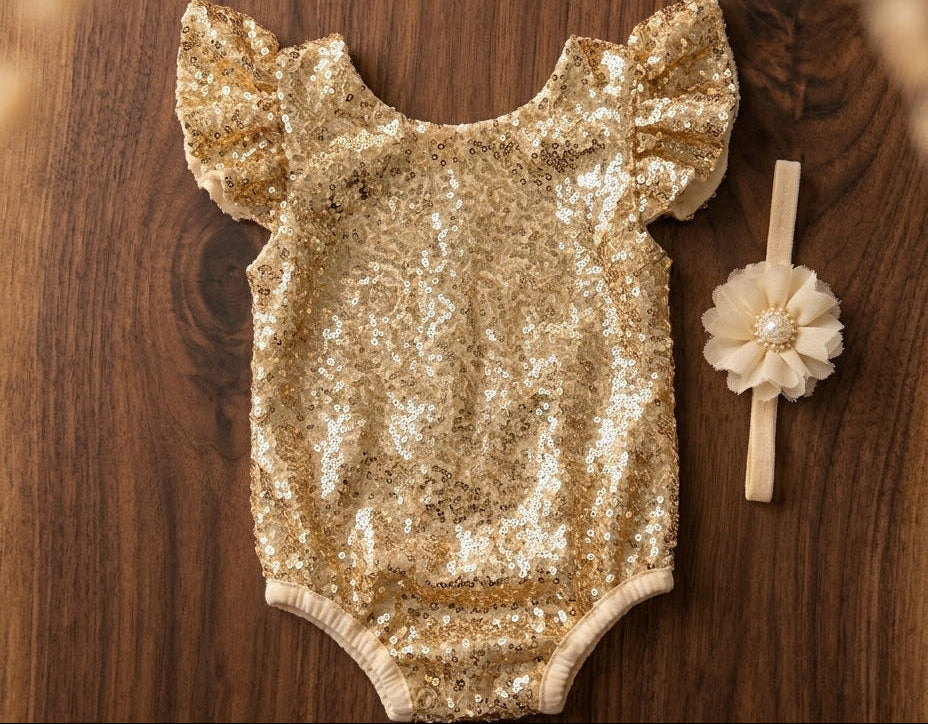 A gold sequined baby bodysuit with ruffled sleeves and an ivory flower headband.